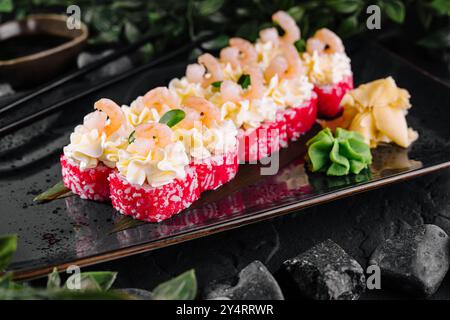 Exquisite Sushi-Brötchen mit Garnelen, Kaviar und cremiger Sauce auf einem eleganten schwarzen Teller Stockfoto