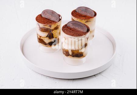 Drei einzelne Portionen Tiramisu in klaren Gläsern, wunderschön präsentiert auf einem runden weißen Teller Stockfoto