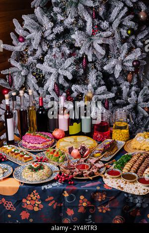 Üppiger Feiertagstisch mit einer Auswahl an Gerichten vor einem wunderschön dekorierten weihnachtsbaum Stockfoto