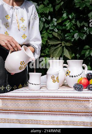 Die Person serviert ein Getränk aus einem Keramikkrug in eine Tasse auf einem Tisch mit ethnischer Einrichtung Stockfoto