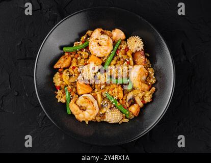 Blick von oben auf ein herzhaftes Garnelenbraten mit gemischtem Gemüse und Reis, serviert auf einem dunklen Teller Stockfoto