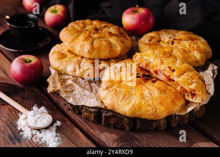 Frisch gebackenes, gefülltes Gebäck mit roten Äpfeln und Kaffee auf hölzernem Hintergrund Stockfoto