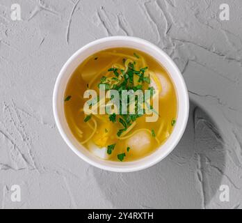 Blick von oben auf eine gemütliche Schüssel mit Hühnernudelsuppe, garniert mit Petersilie auf einer strukturierten Oberfläche Stockfoto