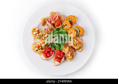 Blick von oben auf eine Vielzahl von Bruschetta mit frischen Zutaten auf einem runden Teller, isoliert auf weiß Stockfoto