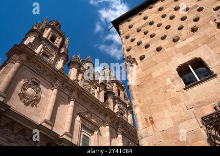 Seitlicher Blick auf La Casa de las Conchas und die Kirche Clerecía entlang der Straße in Salamanca, die Architektur unter hellem Himmel hervorhebt. Stockfoto