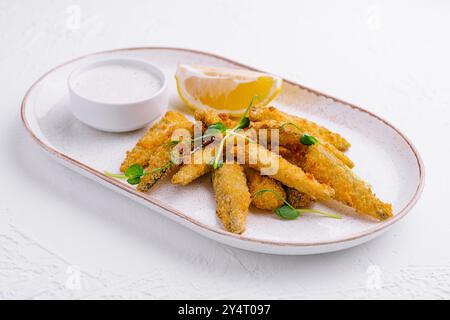 Goldene Fischfinger, serviert mit einer Beilage von Zitrone und cremiger Tatarensauce auf einer Keramikplatte Stockfoto