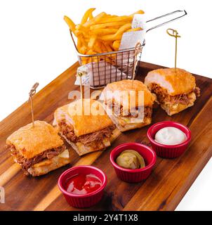 Köstliche Mini-Burger serviert mit goldenen Pommes frites und einer Auswahl an Saucen auf einem Holzbrett Stockfoto