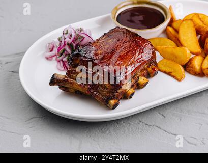Köstlicher Teller mit glasierten Schweinerippchen mit Kartoffelscheiben, bbq-Sauce und Slaw auf einem weißen Teller Stockfoto