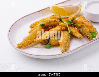 Goldene Fischfinger, serviert mit einer Beilage von Zitrone und cremiger Tatarensauce auf einer Keramikplatte Stockfoto