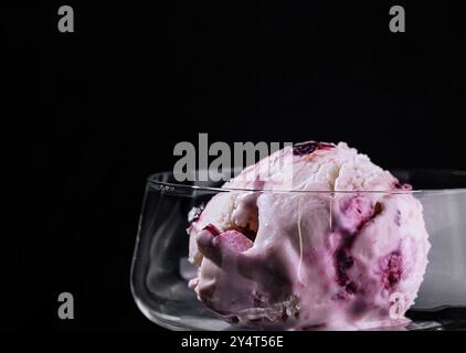 Verwöhnen Sie sich mit einem einzelnen Messlöffel Beereneis, das in einem eleganten Stängelglas vor dunkler Kulisse präsentiert wird Stockfoto