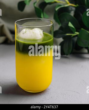 Leuchtend grüner Matcha schweben neben einem Glas frischen Mangofrests auf einem schicken grauen Hintergrund Stockfoto