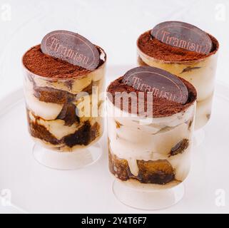 Drei einzelne Portionen Tiramisu in klaren Gläsern, wunderschön präsentiert auf einem runden weißen Teller Stockfoto