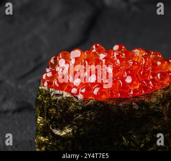 Einzelnes Stück Lachsrogen Sushi elegant auf einem strukturierten dunklen Schieferhintergrund angeordnet Stockfoto