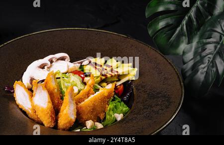 Exquisiter gebratener Hähnchensalat mit frischem Gemüse und Avocado, serviert auf einem dunklen Teller mit stilvoller Präsentation Stockfoto