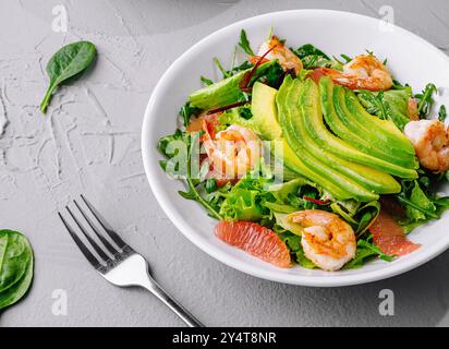 Schüssel mit lebendigem Garnelenavocadosalat, perfekt für gesunde Ernährung, auf einem grauen strukturierten Hintergrund Stockfoto