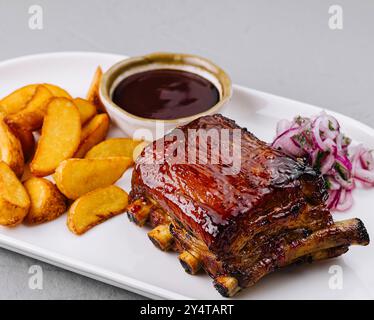 Köstlicher Teller mit glasierten Schweinerippchen mit Kartoffelscheiben, bbq-Sauce und Slaw auf einem weißen Teller Stockfoto