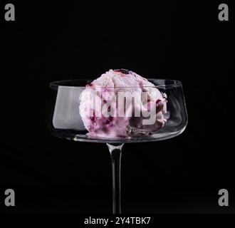 Verwöhnen Sie sich mit einem einzelnen Messlöffel Beereneis, das in einem eleganten Stängelglas vor dunkler Kulisse präsentiert wird Stockfoto