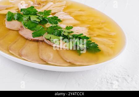 Hausgemachte Hühneraspik mit Fleischscheiben und frischer Petersilie auf weißem Hintergrund Stockfoto