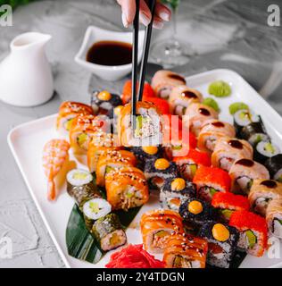 Nahaufnahme einer Person, die Essstäbchen verwendet, um eine Sushi-Rolle von einer verschiedenen Platte zu holen Stockfoto