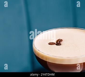 Eleganter Espresso-Martini mit Kaffeebohnen, serviert auf einem weißen Tisch vor blauem Hintergrund Stockfoto