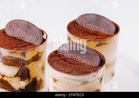 Drei einzelne Portionen Tiramisu in klaren Gläsern, wunderschön präsentiert auf einem runden weißen Teller Stockfoto