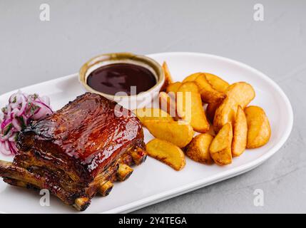 Köstlicher Teller mit glasierten Schweinerippchen mit Kartoffelscheiben, bbq-Sauce und Slaw auf einem weißen Teller Stockfoto