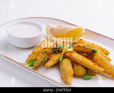 Goldene Fischfinger, serviert mit einer Beilage von Zitrone und cremiger Tatarensauce auf einer Keramikplatte Stockfoto
