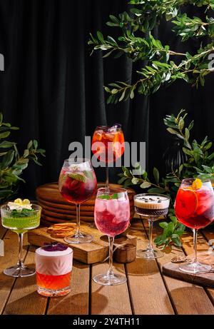 Vielfältige Auswahl an Cocktails, die künstlerisch vor einer dunklen, eleganten Kulisse mit Grün präsentiert werden Stockfoto