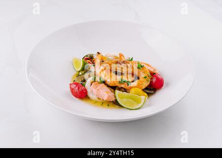 Weißer Teller präsentiert eine herzhafte Pasta mit Meeresfrüchten und frischer Limette auf Marmorhintergrund Stockfoto