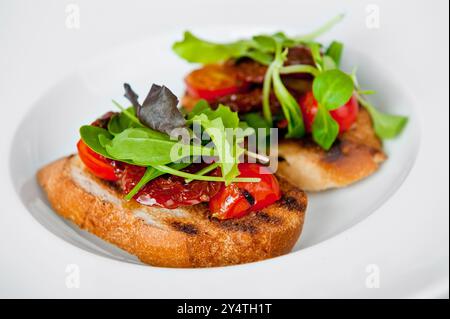 Appetitliche Bruschetta mit Kirschtomaten, Salatblättern und einem würzigen Dressing auf einem weißen Teller Stockfoto