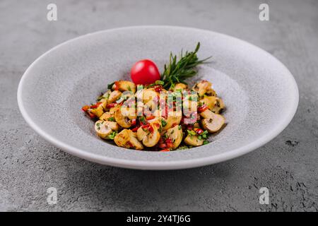 Frisch gebratene Pilze mit Kräutern, garniert mit einer Kirschtomate in einer Keramikschale Stockfoto