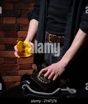 Teilbetrachtung einer Person, die an einem Tisch steht, einen Apfelsaft hält und ein antikes Telefon wählt Stockfoto