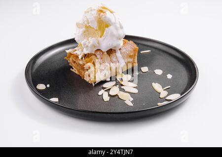apfelstrudel mit Vanilleeis und Mandeln, serviert auf einem modernen schwarzen Teller Stockfoto