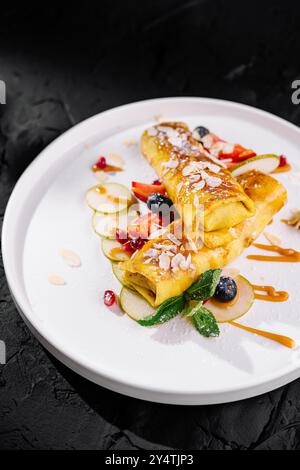 Kunstvoll beschichtete Crepes mit Fruchtbelag und Karamellbesatz auf dunklem Hintergrund Stockfoto