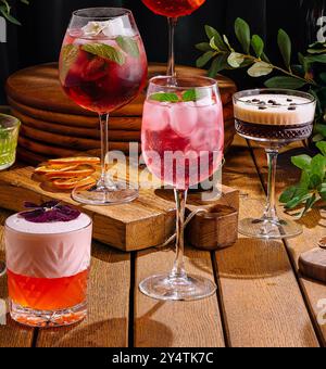 Vielfältige Auswahl an Cocktails, die künstlerisch vor einer dunklen, eleganten Kulisse mit Grün präsentiert werden Stockfoto