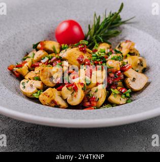 Frisch gebratene Pilze mit Kräutern, garniert mit einer Kirschtomate in einer Keramikschale Stockfoto