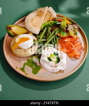 Köstlicher Brunch-Teller mit pochiertem Ei, geräuchertem Lachs, Avocado und frischem Gemüse auf einem trendigen Keramikgericht Stockfoto