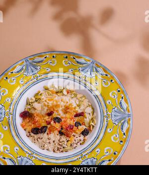 Blick von oben auf eine nahrhafte Müslimischung mit getrockneten Früchten und Nüssen in einer lebendigen Keramikschale vor pastellfarbenem Hintergrund Stockfoto