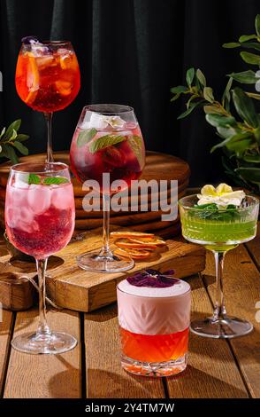 Vielfältige Auswahl an Cocktails, die künstlerisch vor einer dunklen, eleganten Kulisse mit Grün präsentiert werden Stockfoto