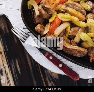 Saftiges Rindfleisch, gebraten mit Gemüse in einer Pfanne, serviert auf rustikalem Holzhintergrund Stockfoto