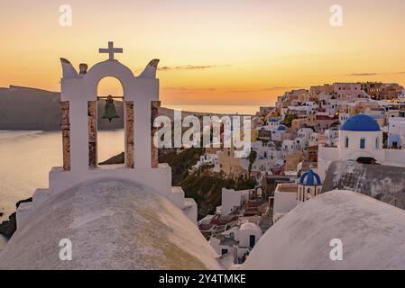 Blaue Kuppelkirchen und Glockenturm mit Blick auf die Ägäis mit warmem Sonnenuntergangslicht in Oia, Santorin, Griechenland, Europa Stockfoto