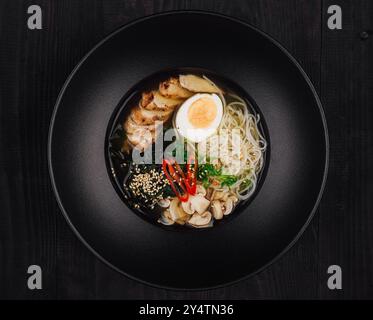 Eine köstliche Schüssel Hühnerramen wird in einer schwarzen Schüssel auf einem schwarzen Tisch serviert Stockfoto