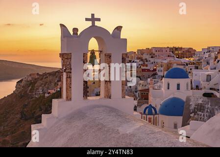 Blaue Kuppelkirchen und Glockenturm mit Blick auf die Ägäis mit warmem Sonnenuntergangslicht in Oia, Santorin, Griechenland, Europa Stockfoto