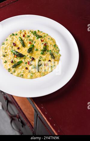 Cremiges Risotto mit Spargel und Pancetta, serviert auf einem weißen Teller auf einem Holztisch Stockfoto