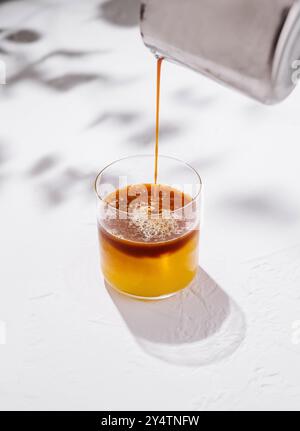 Der Barkeeper gießt einen Espresso in ein Glas mit einem gelben Cocktail auf weißem Hintergrund Stockfoto