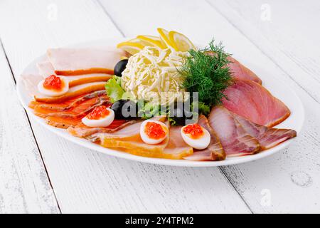 Auf einem weißen Holztisch wird eine in Scheiben geschnittene Fischplatte mit Butter, Zitrone und Oliven serviert Stockfoto