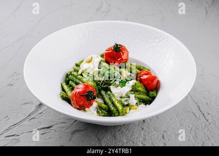 Köstliche vegetarische Mahlzeit mit Trofie-Pasta und Basilikum-Pesto-Sauce, dekoriert mit Pinienkernen, gebackenen Kirschtomaten und Burrata-Käse, serviert auf weiß Stockfoto