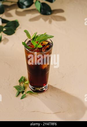 Auf einem Tisch steht ein hohes Glas mit einem erfrischenden dunklen Cocktail, der mit frischen Minzblättern dekoriert ist Stockfoto