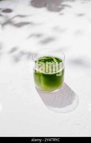Erfrischende Eismatcha Latte sitzt auf einem weißen Tisch mit Schatten von Blättern im Hintergrund Stockfoto