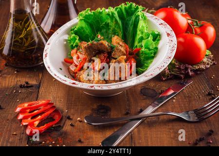 Die weiße Platte enthält eine Portion Rindereintopf aus Tomaten und Zwiebeln, garniert mit Salat Stockfoto